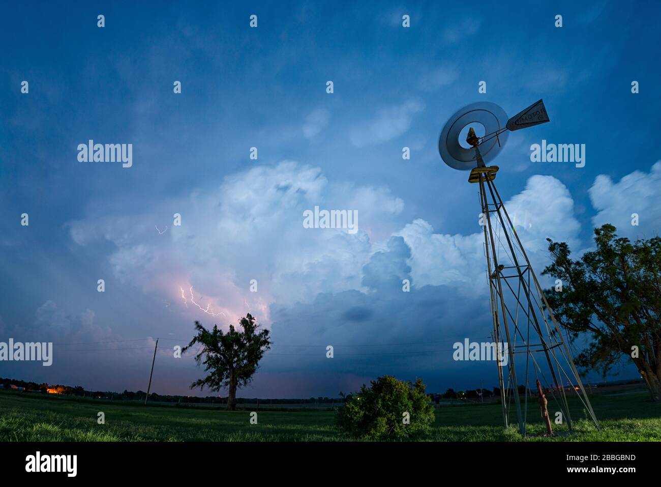 Storm with cloud to cloud lightning flashing over old farm windmill in Texas United States Stock Photo
