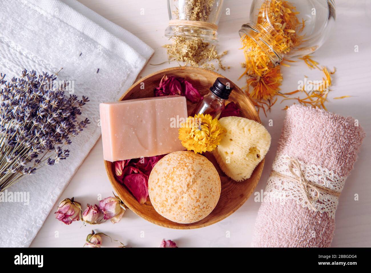 Various organic dried herbs flower petals used in beauty bath products concept. Top view of bath bomb, natural sea sponge, bar of soap, aroma oil. Stock Photo