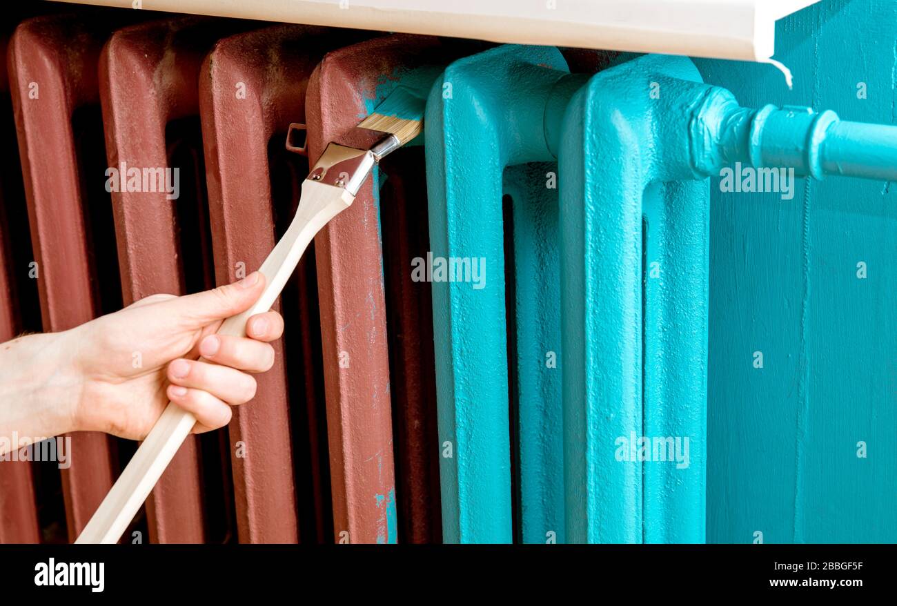 Home refreshing renovation concept. Close up view of man hand painting with special curved radiator paint brush. Stock Photo