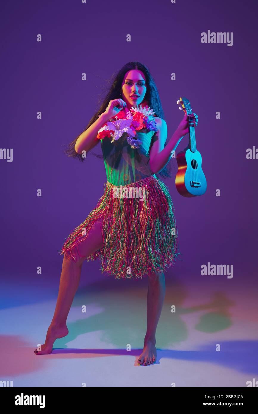Fabulous Cinco de Mayo female dancer on purple studio background in neon light. Beautiful female model with ukulele, Mexico, Hawaii style. Celebration, holiday, music, beauty and fashion concept. Stock Photo