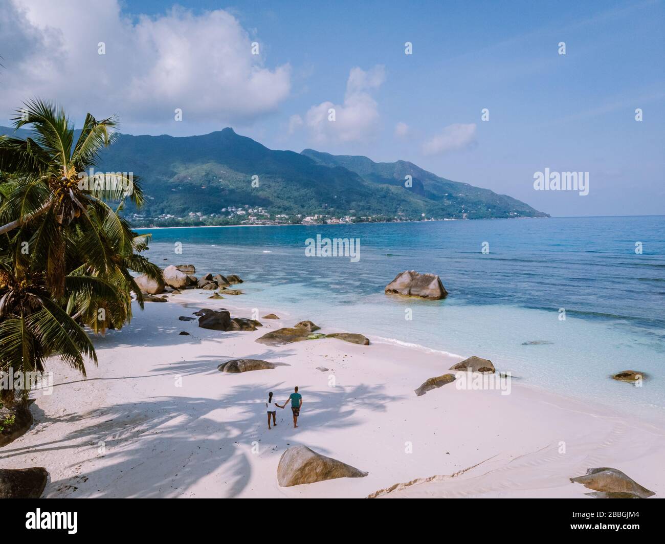 Tropical white beach at Praslin island Seychelles, happy Young couple man and woman during vacation Holiday at the beach relaxing under a palm tree Stock Photo