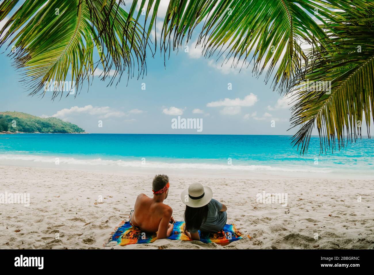 Tropical white beach at Praslin island Seychelles, happy Young couple man and woman during vacation Holiday at the beach relaxing under a palm tree Stock Photo