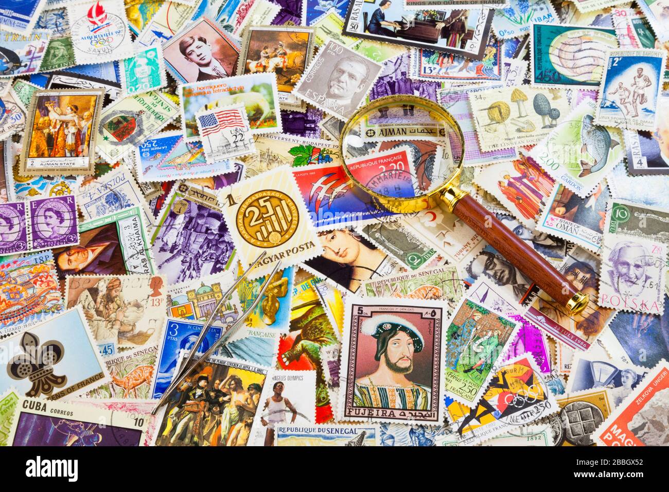 A magnifying glass and a stamp tongs on the top of a stack of worldwide stamps. Stock Photo