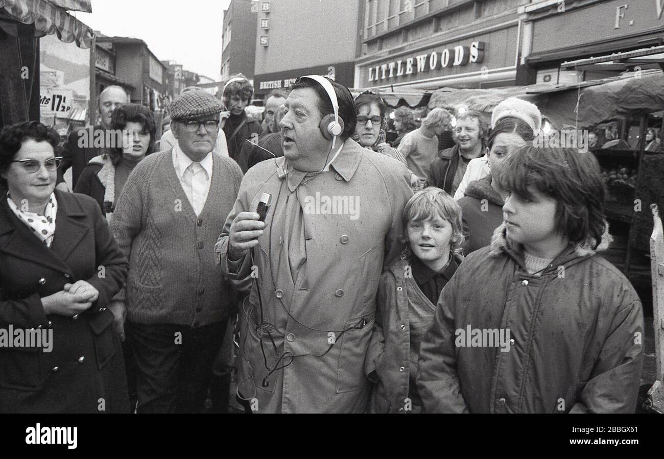 1970s, popular, man of the people, radio presenter and reporter Monty Modlyn in a high street in South London, as he looks for someone to interview. Born into a Jewish family from Lambeth, Modlyn was known for his cockney accent and his broadcast forte was interviewing ordinary people, a technique that became known as 'Vox Pop'. Addressing people with the words 'Ullo darlin', his east end working class persona saw him have conversations about anything and everything during a long and distinguished broadcasting career in both television and radio, both for the BBC and commercial radio. Stock Photo