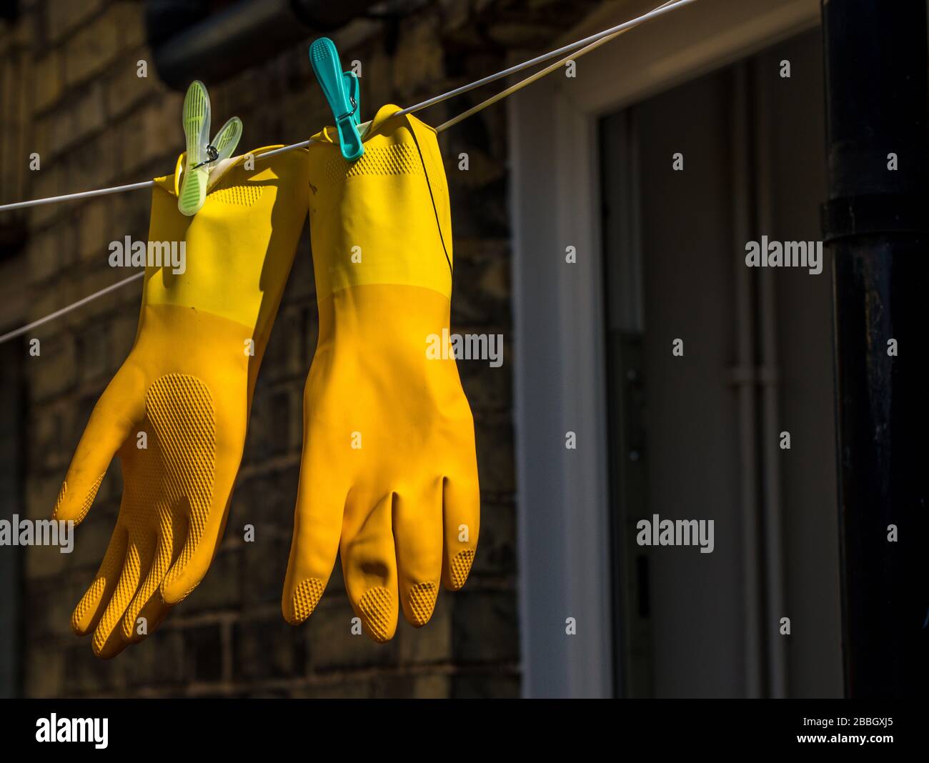 A pair of yellow marigold protective rubber gloves pegged on a clothes line Stock Photo