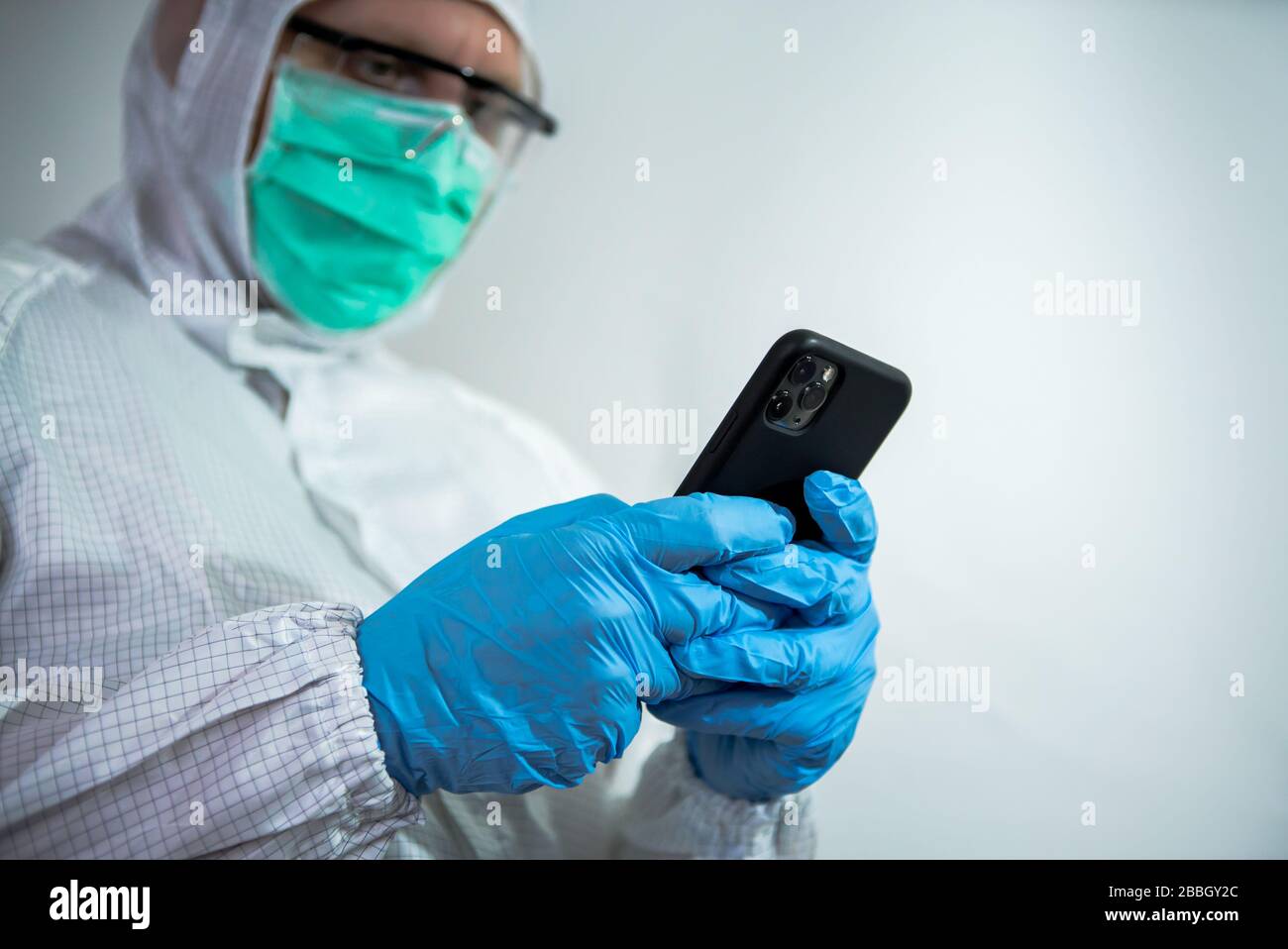 Caucasian man wearing a protective suit and face mask using smartphone on laboratory. Doctor using phone device. Coronavirus has caused emergency situ Stock Photo