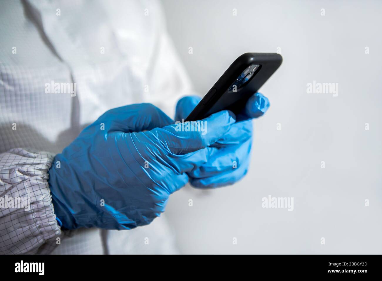 Man wearing a protective suit and blue gloves using smartphone on laboratory. Doctor using phone device. Coronavirus has caused emergency situation. C Stock Photo