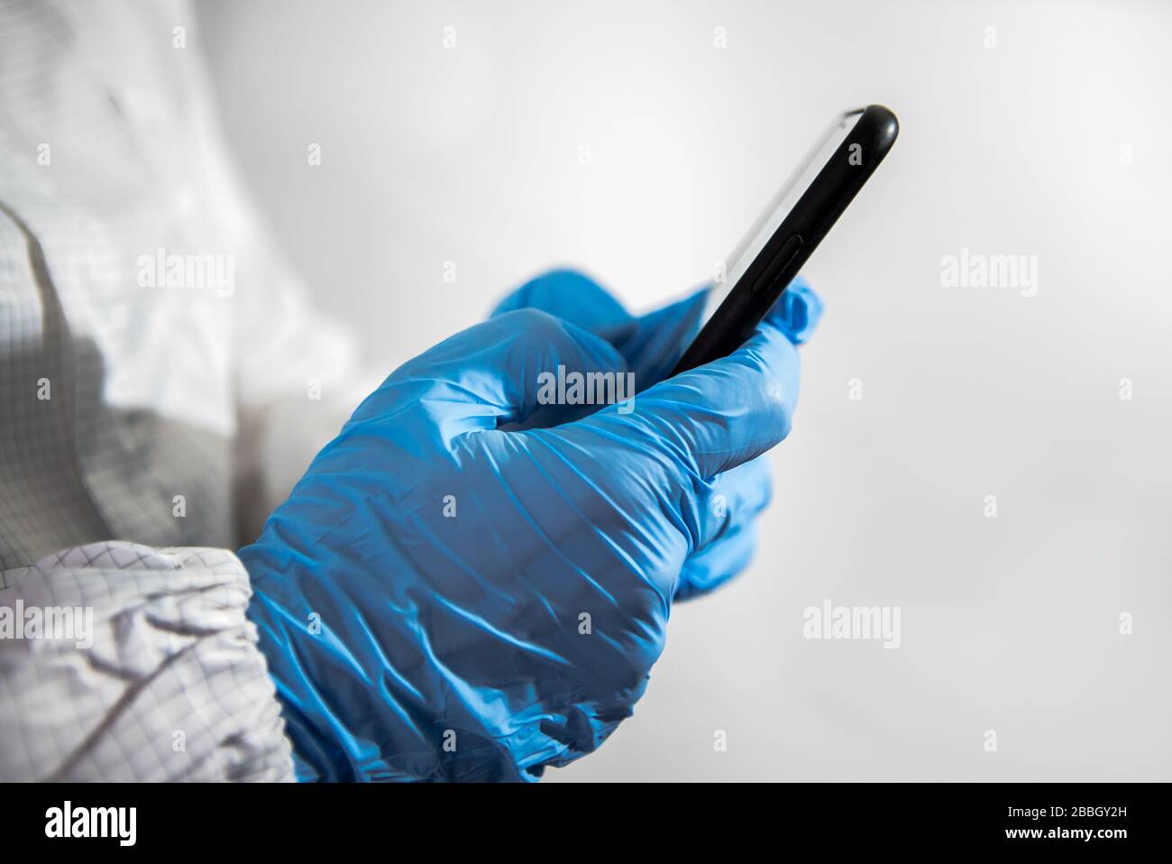 Scientist using smartphone in the scientific chemical laboratory. Doctor hands with blue gloves using phone device. Coronavirus has caused emergency s Stock Photo