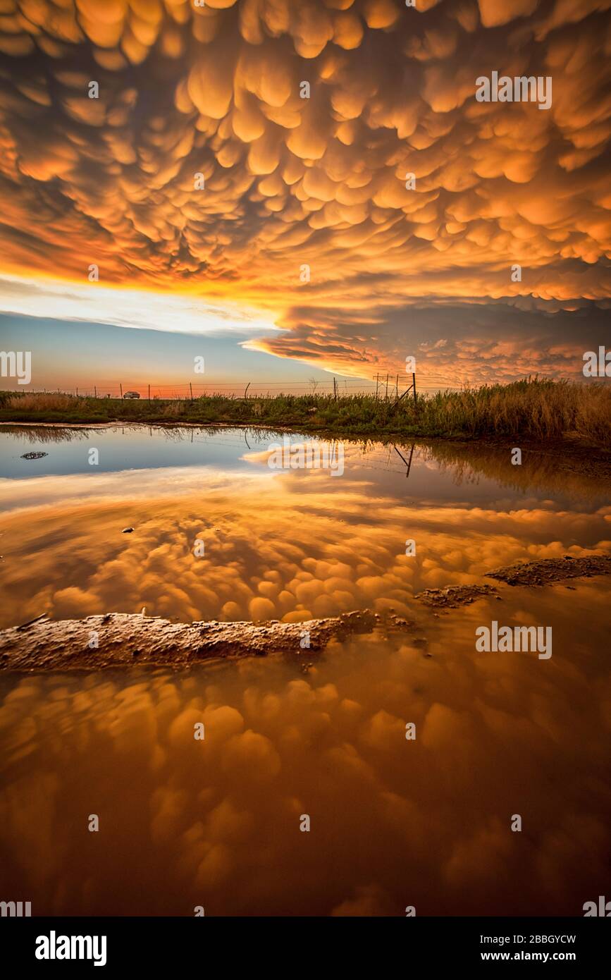 Sunset over a pond with a perfect reflection of bright orange manmatus as the storm passes in Dodge City Kansas United States Stock Photo
