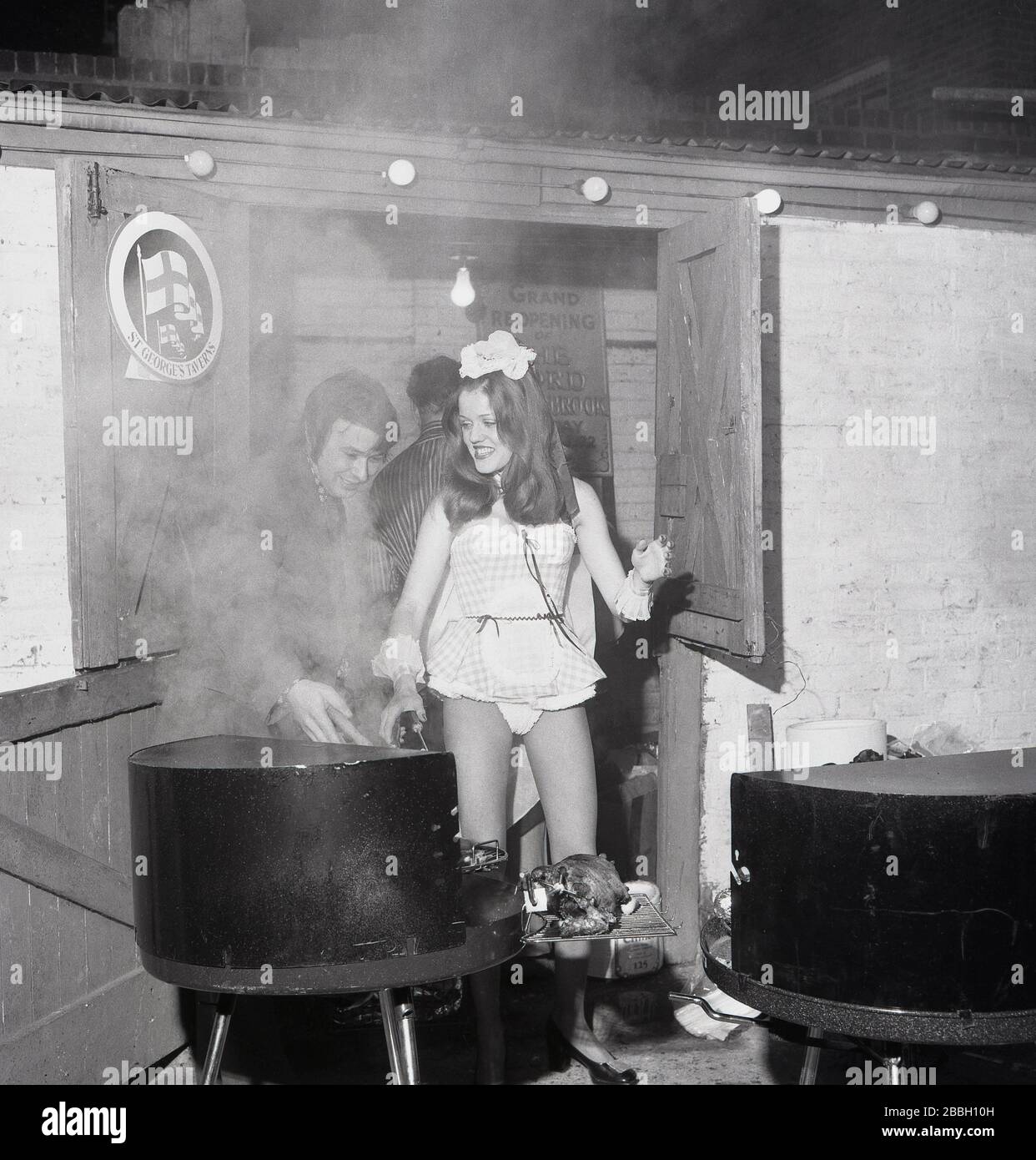 1973, historical, an attractive young lady wearing a very short party frock helping with the cooking outside on a grill at a fund raising barbeque at The Lord Northbrook pub, Lee, South East London, England. At the corner of southbrook Rd, the pub is named after Lord Northbrook, whose family, Baring, the banking family in the 19th century had an estate in the borough. Stock Photo