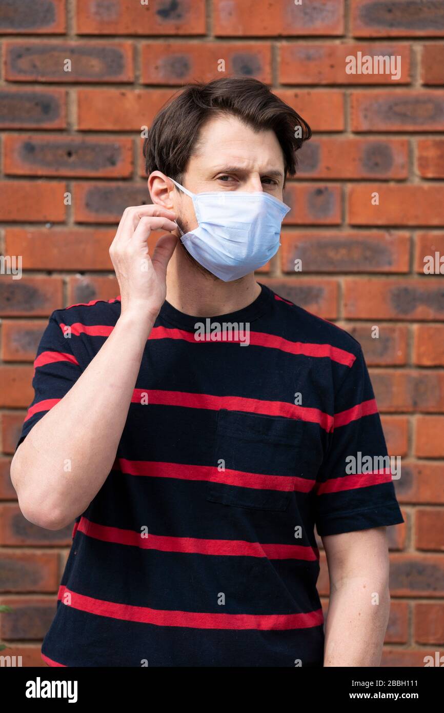 Mid 40's casual male wears blue face mask at height of Coronavirus outbreak, against brick wall. Stock Photo