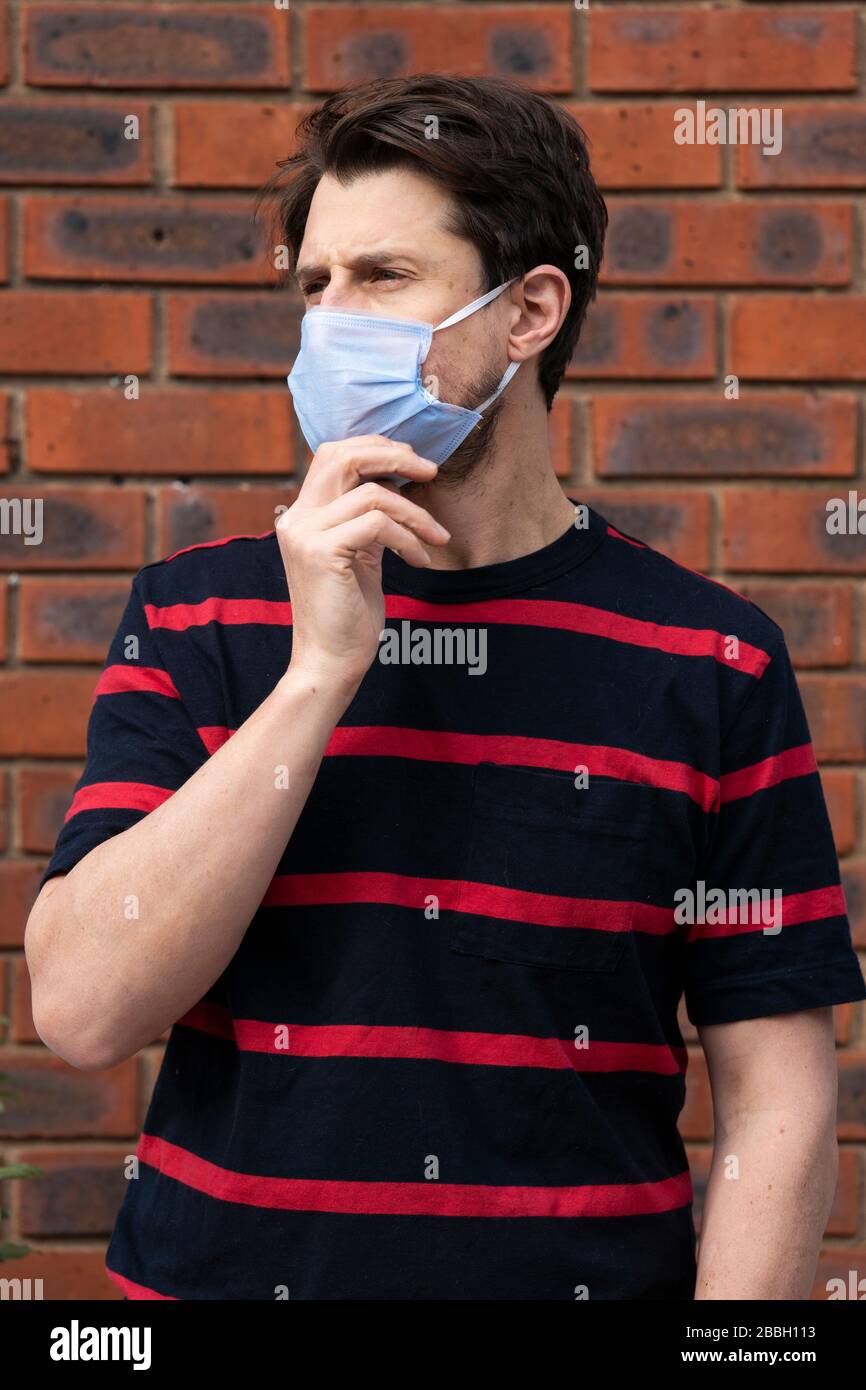 Mid 40's casual male wears blue face mask at height of Coronavirus outbreak, against brick wall. Stock Photo