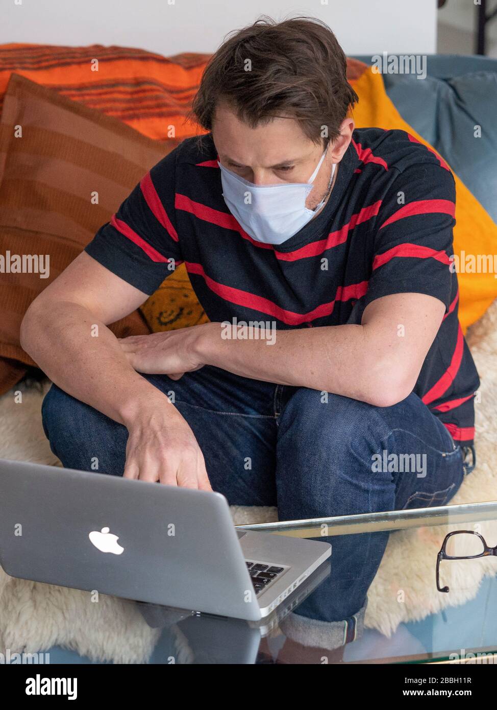 Mid 40's male working from home with Apple laptop, wearing face mask. Stock Photo