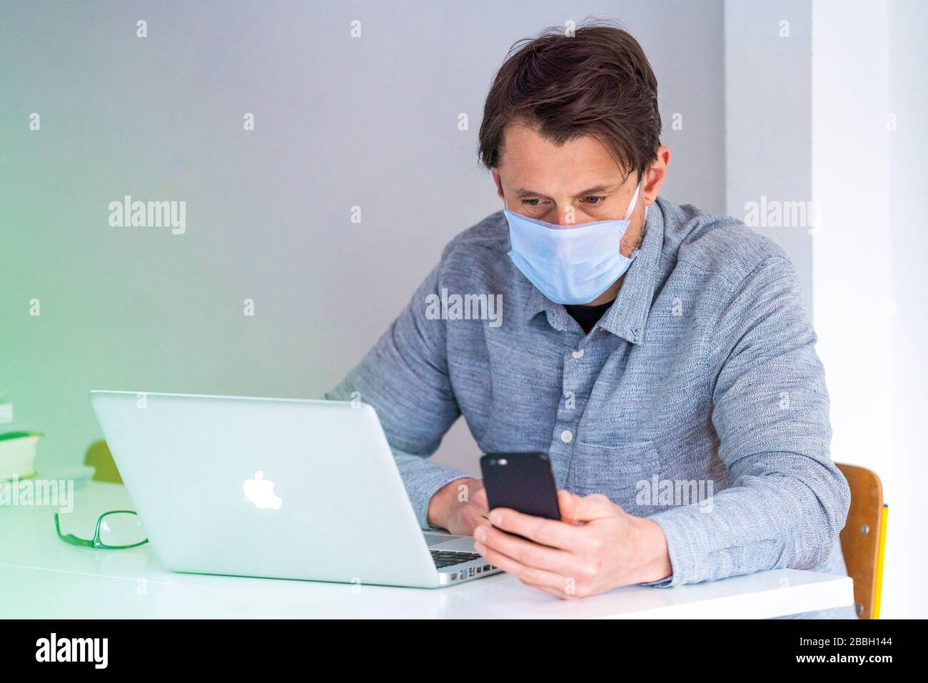 Mid 40's male working from home with Apple laptop, wearing face mask. Stock Photo