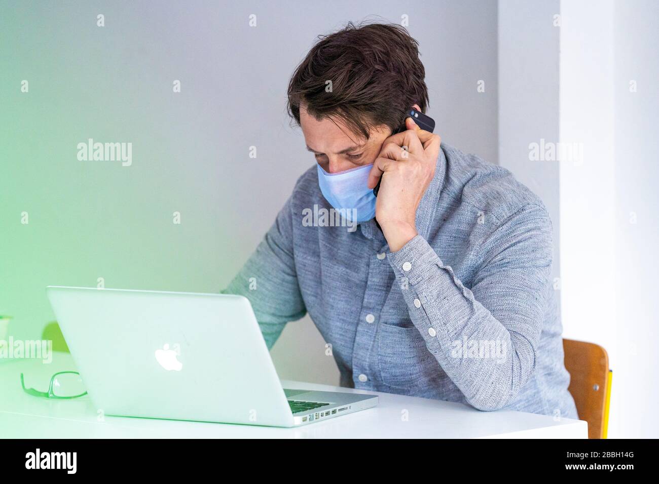 Mid 40's male working from home with Apple laptop, wearing face mask. Stock Photo