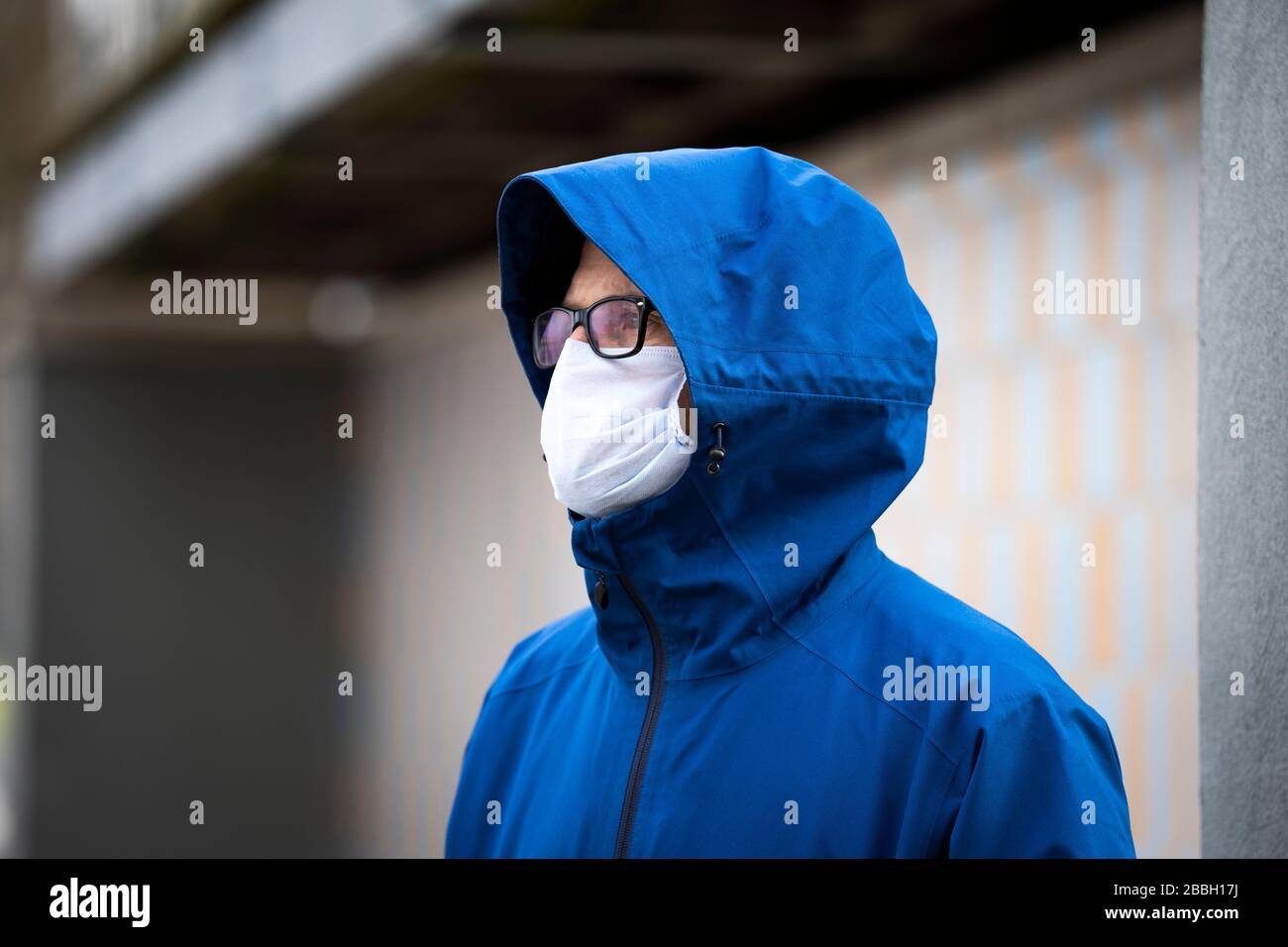 Mid 40's male wearing blue jacket and face mask on the River Thames, London, with yellow and blue background, and concrete. Stock Photo