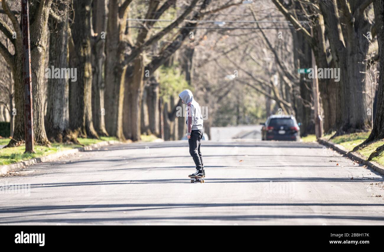 Berks County, Pennsylvania, USA-March 22, 2020: Lone skateboarder on empty tree lined suburban street. Stock Photo