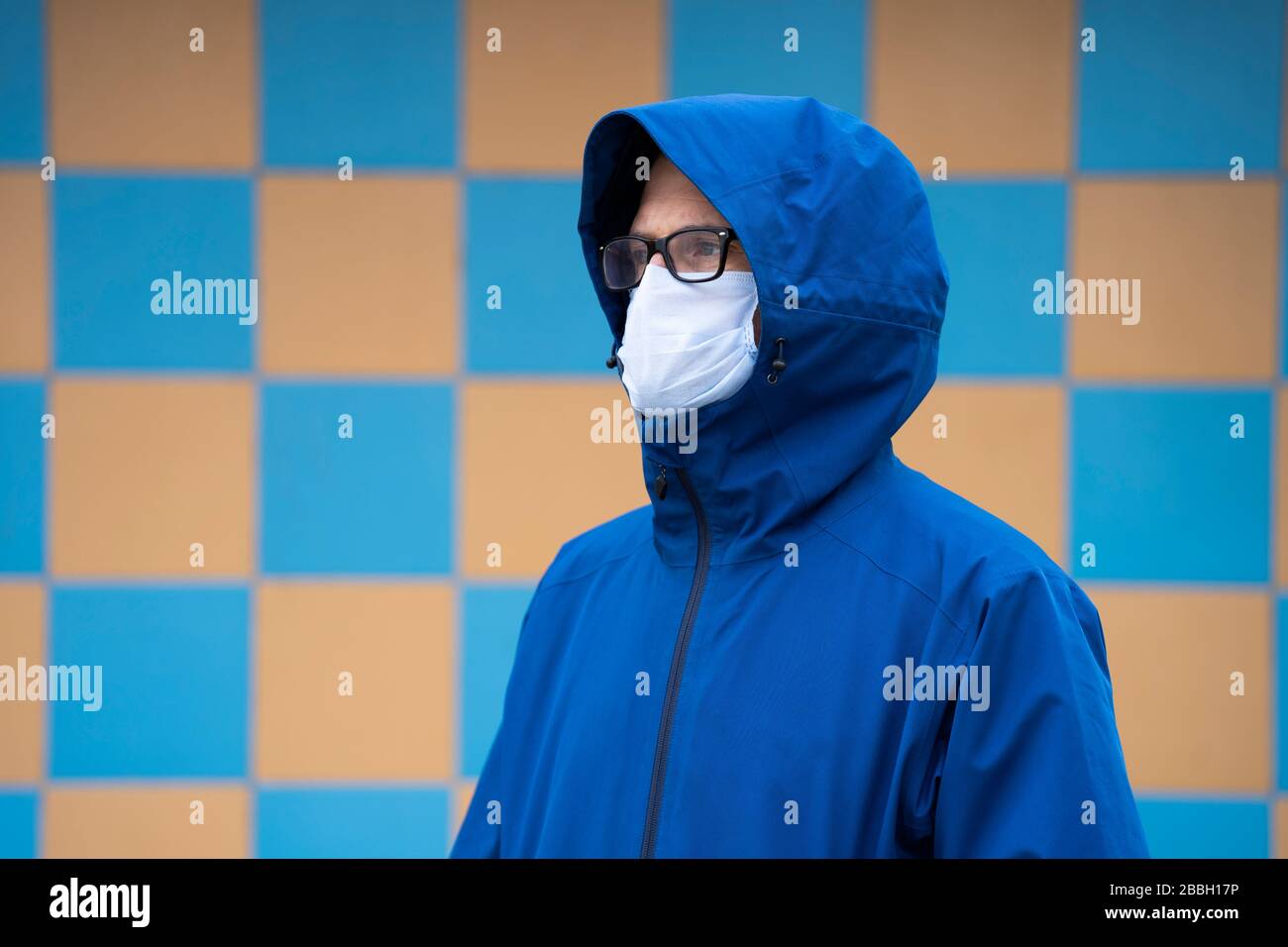 Mid 40's male wearing blue jacket and face mask on the River Thames, London, with yellow and blue background, and concrete. Stock Photo