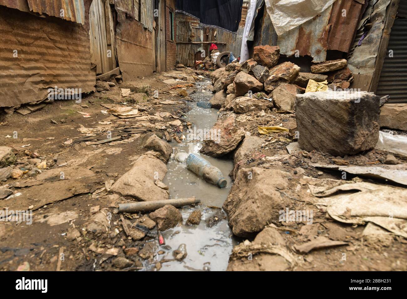 Open sewer running through small alley with metal slum shacks either side, Nairobi, Kenya Stock Photo