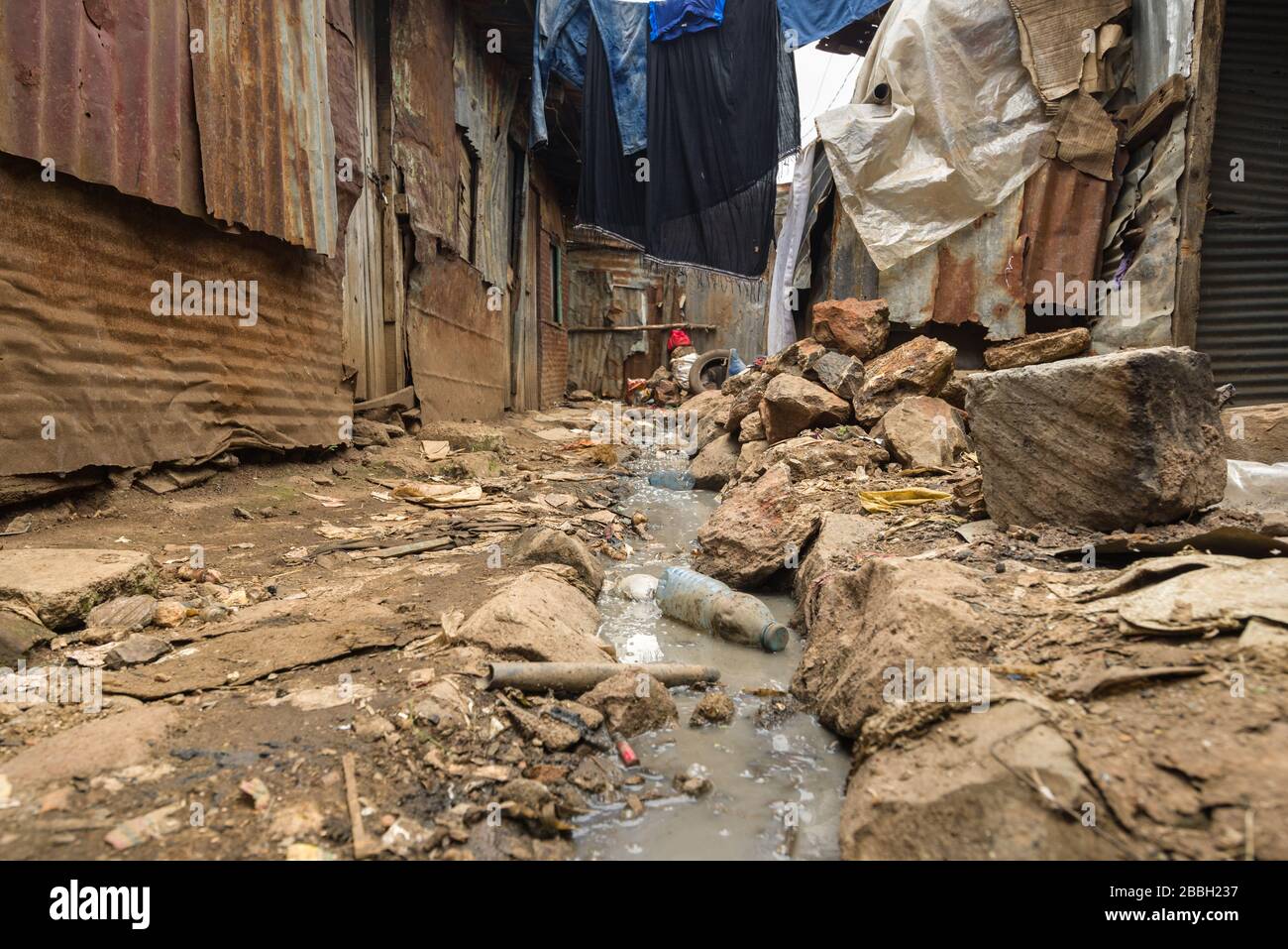 Open sewer running through small alley with metal slum shacks either side, Nairobi, Kenya Stock Photo
