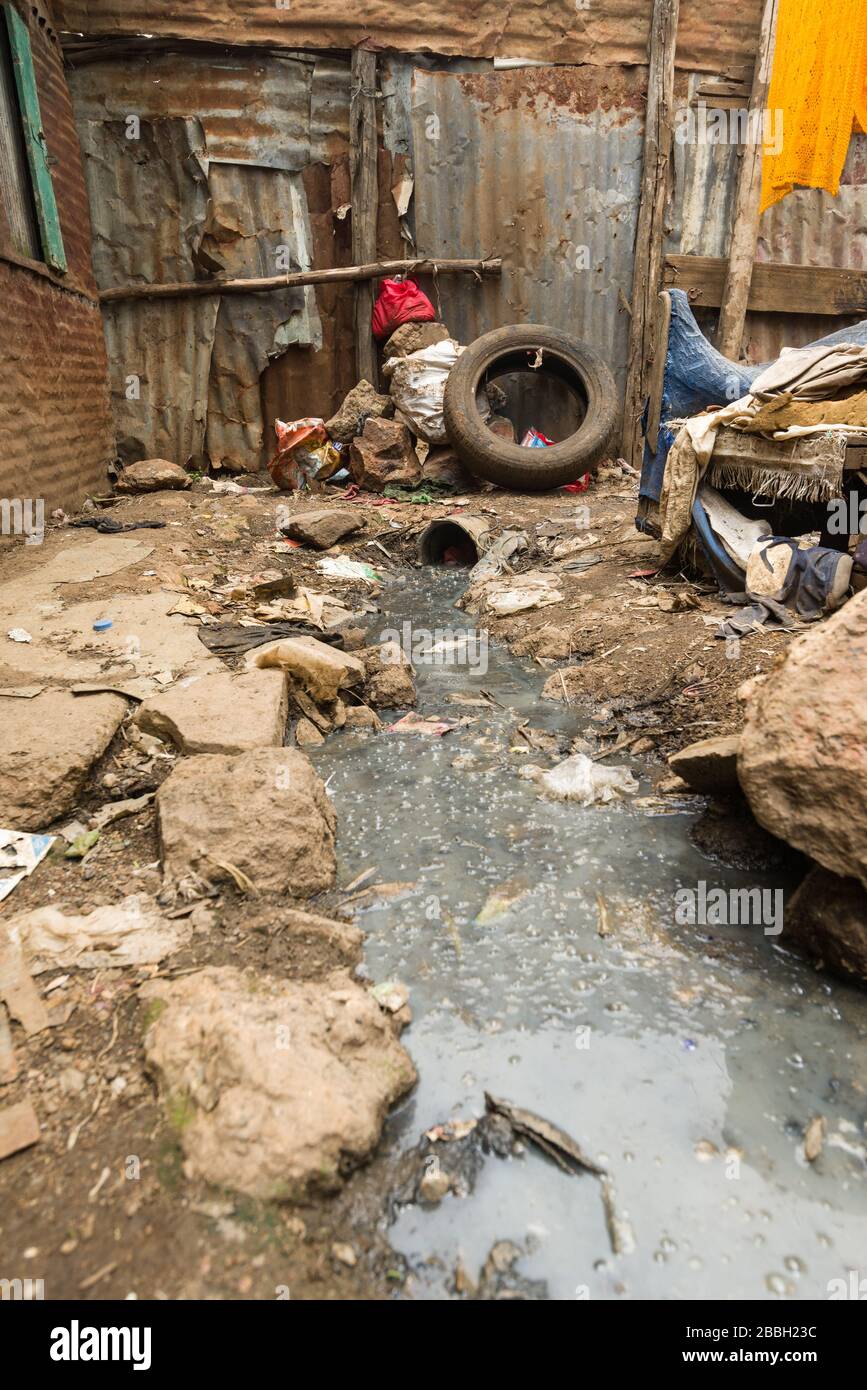 Open sewer running through small alley with metal slum shacks either side, Nairobi, Kenya Stock Photo