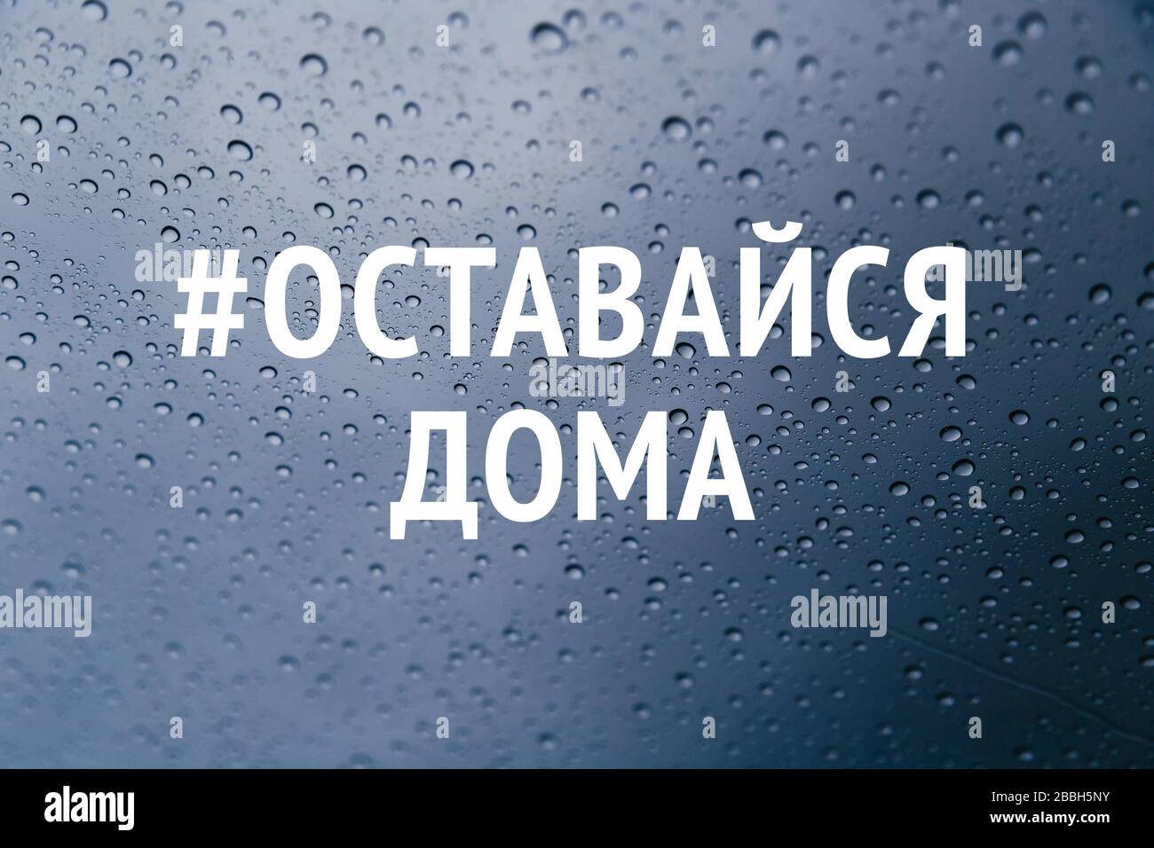 Stay at home in russian language social media campaign for coronavirus prevention. Stay home stay safe concept. Close up of rain drops on the window Stock Photo