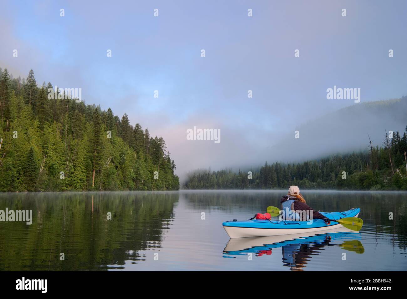 Kayaker with blue kayak on Echo Lake at sunrise, Echo Lake provincial park near Lumby, British Columbia, Canada. Stock Photo