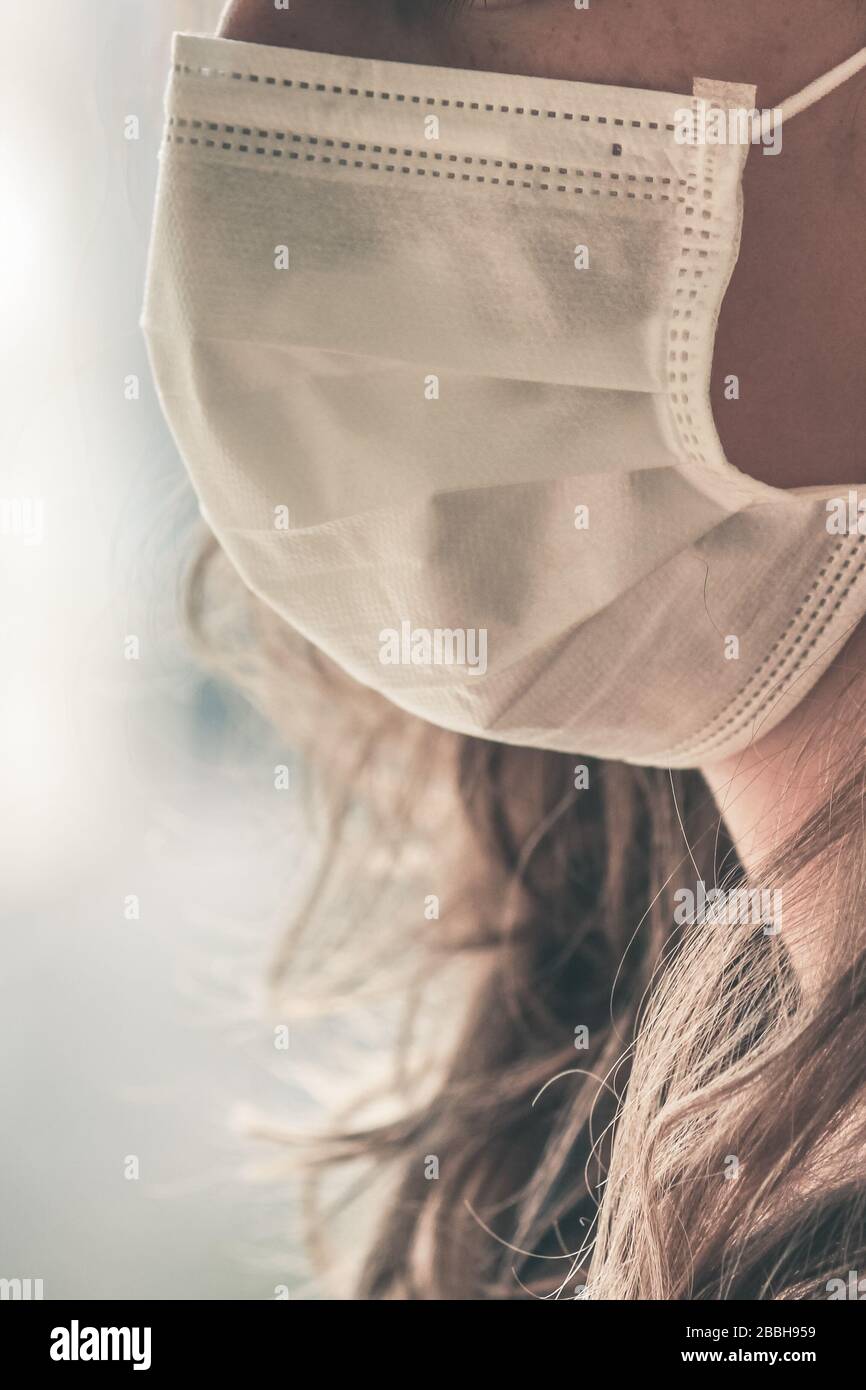 Unrecognizable Caucasian woman wearing a white medical face mask to prevent infection. Focus on the front part of the face, blurred background. Coronavirus, COVID-19 quarantine. Doctor, nurse concept. Stock Photo