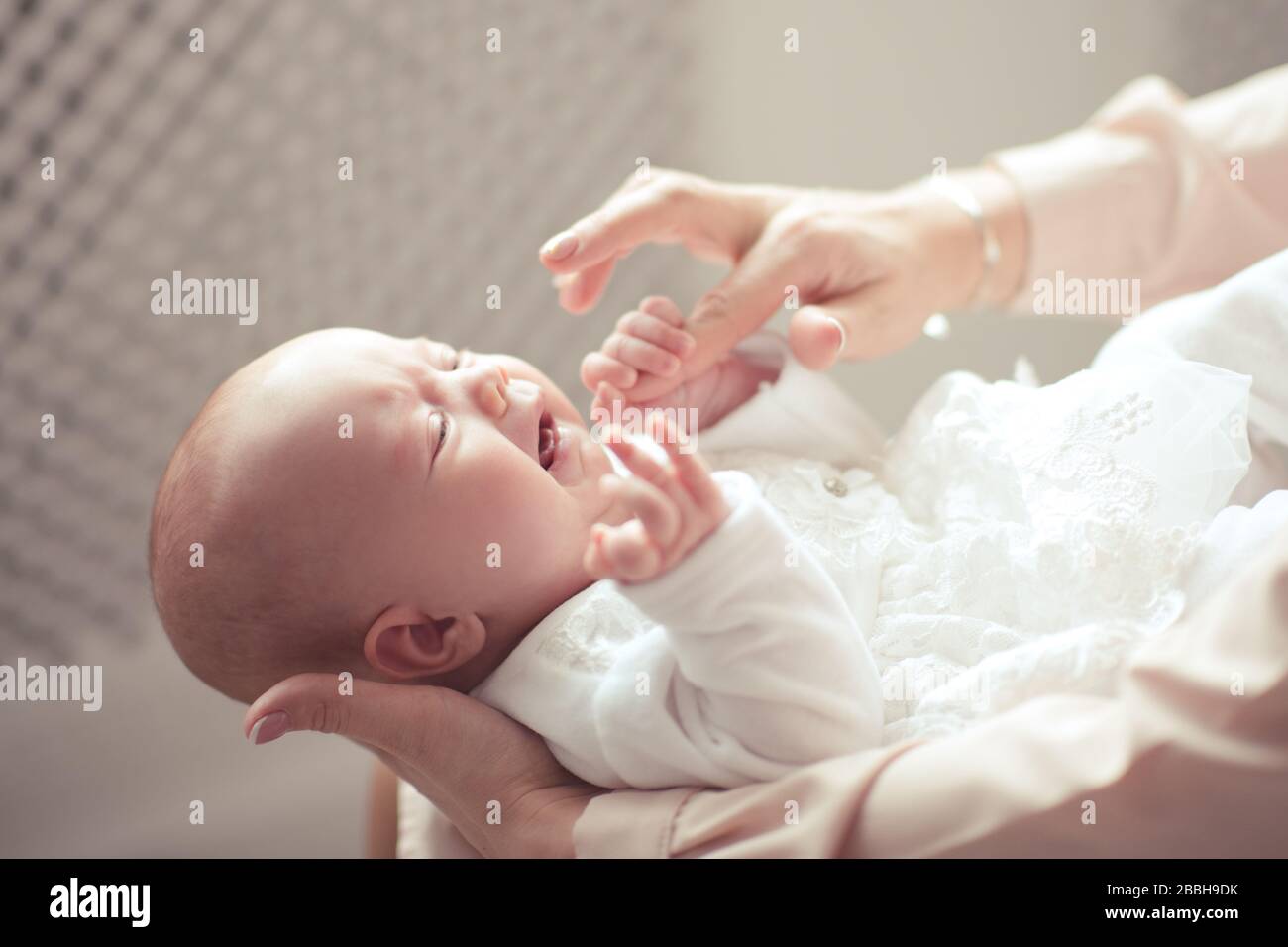 Crying baby girl wake up on mother hands in room closeup. Woman with