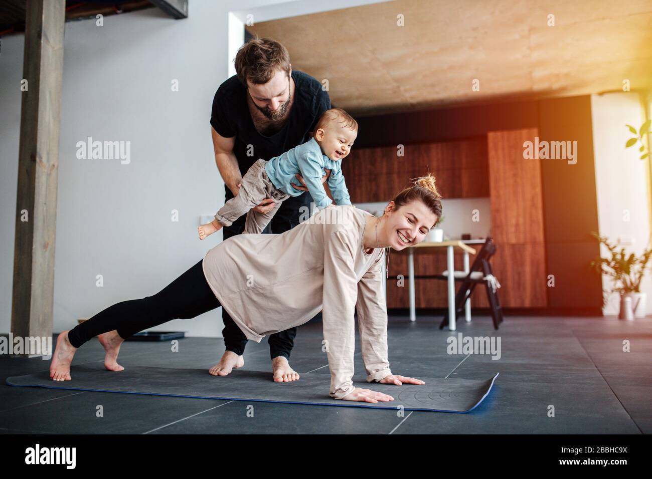 Family morning exercise. Mother doing plank, father holding baby on her back Stock Photo