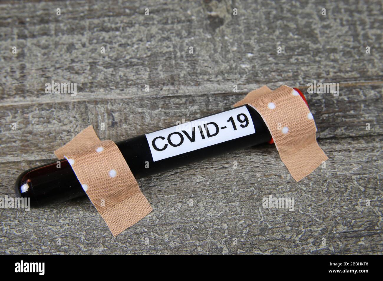 Containing and treatment corona virus epidemic contagion risk concept: Close up of covid-19 blood sample vial fixed with wound plasters on wood table Stock Photo