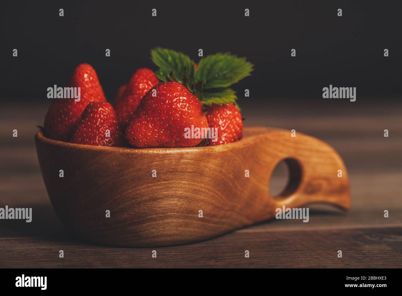 Fresh strawberries with leaves in wooden bowl on rustic brown wooden ...