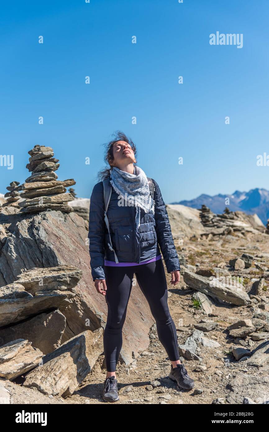 Young white Caucasian woman looking at the sky. Meditating in front of a stone pyramid. Eggishorn terrace, place of energy and power. Stock Photo