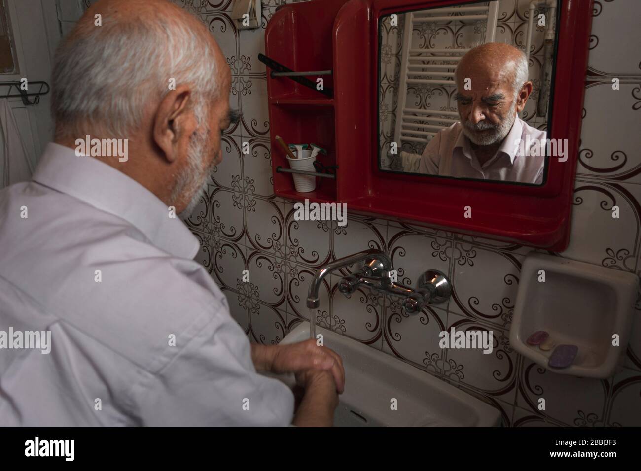 80 years old Turkish man washing his hands in front of his mirror at his retro looking bathroom Stock Photo