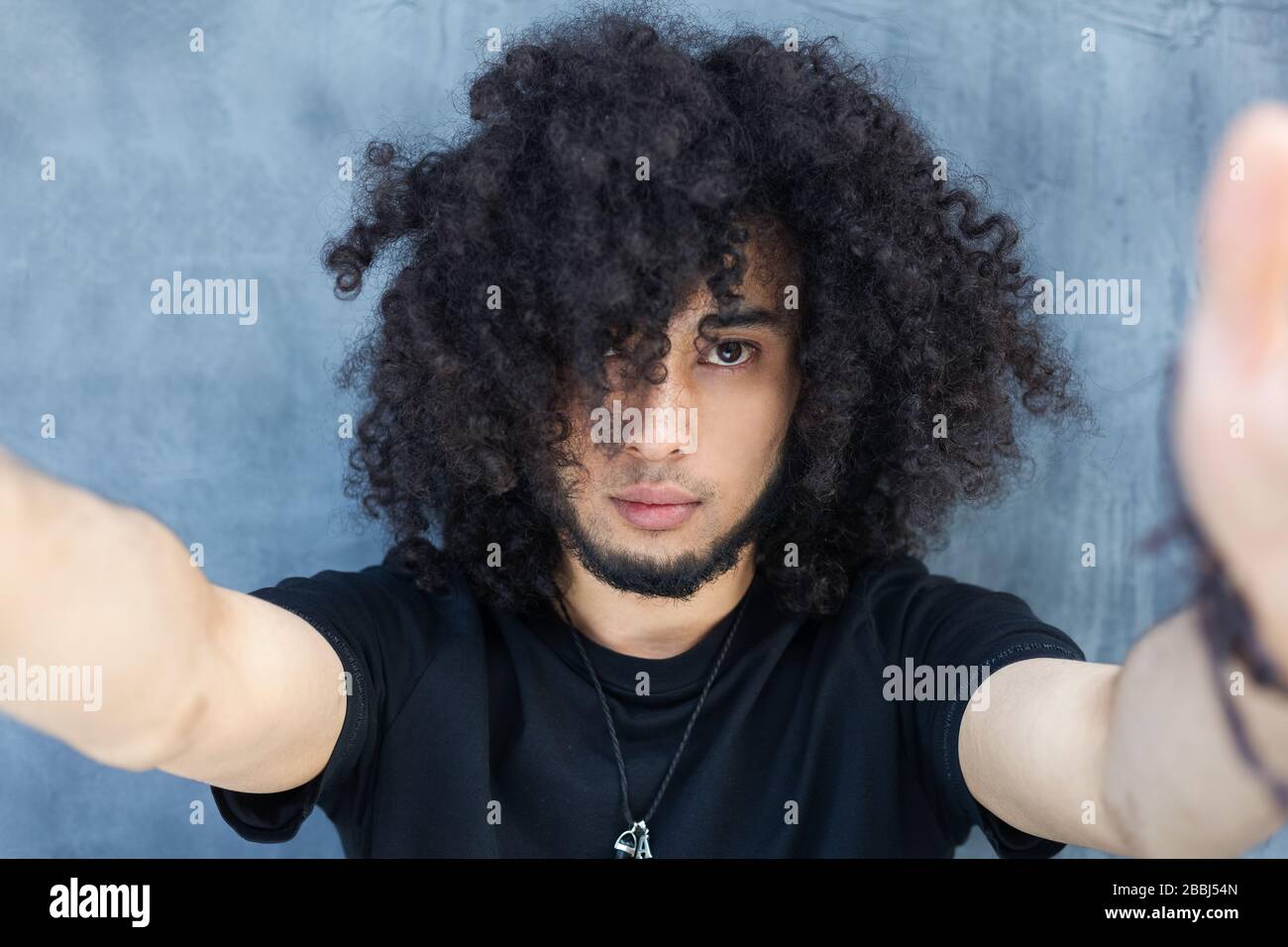 Handsome young African man making selfie while standing against grey background. Afro hair. Stock Photo