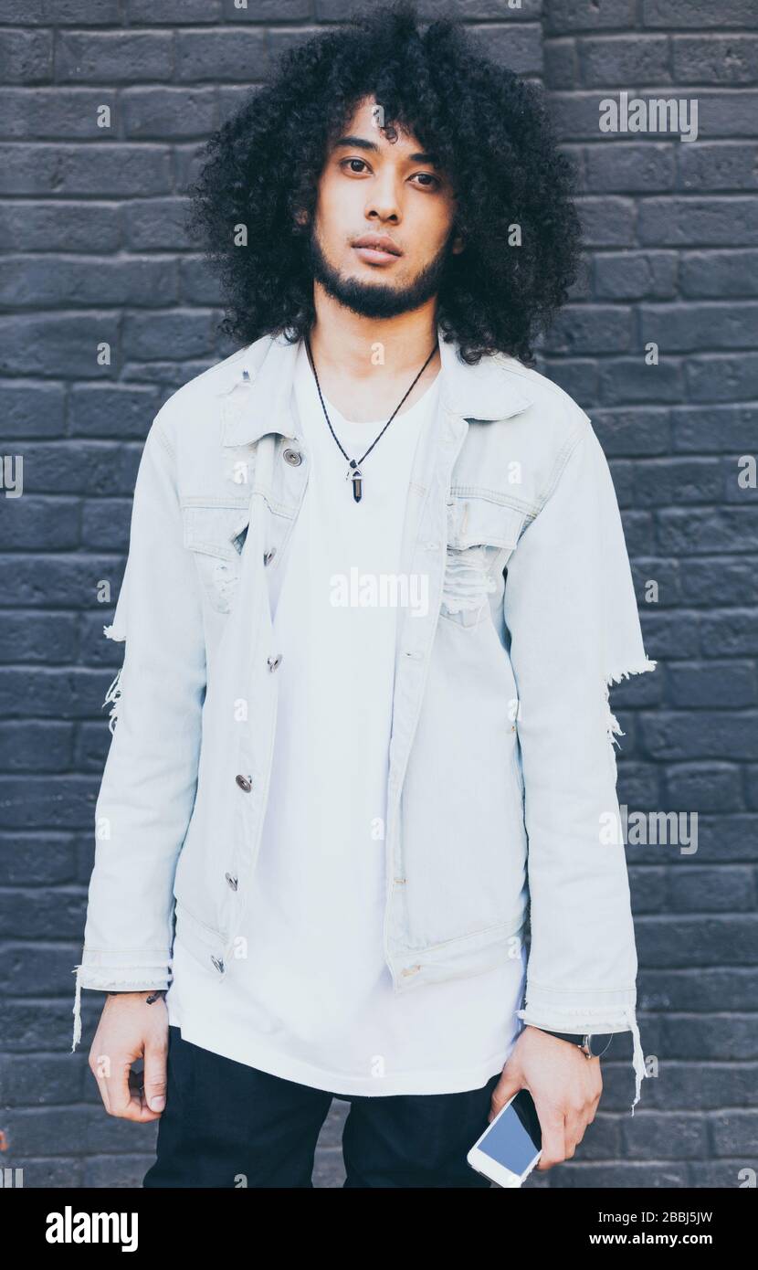 Portrait of handsome young black man with curly afro hair. Outside. Dressed in a jeans jacket, black trousers. Fashion. Street style. Stock Photo