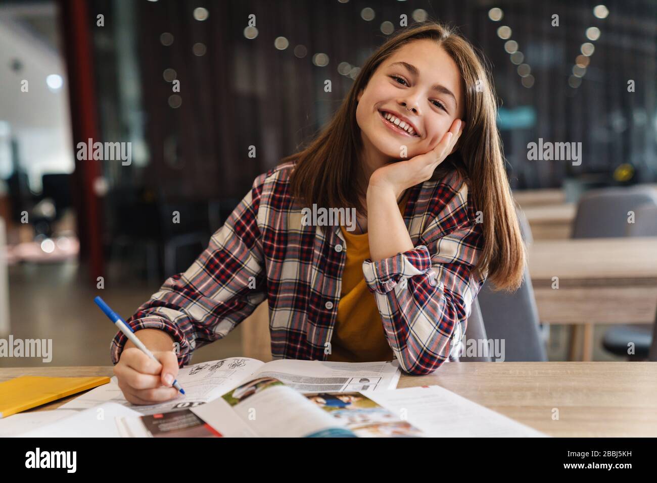 Image of joyful caucasian girl doing homework with exercise books while ...
