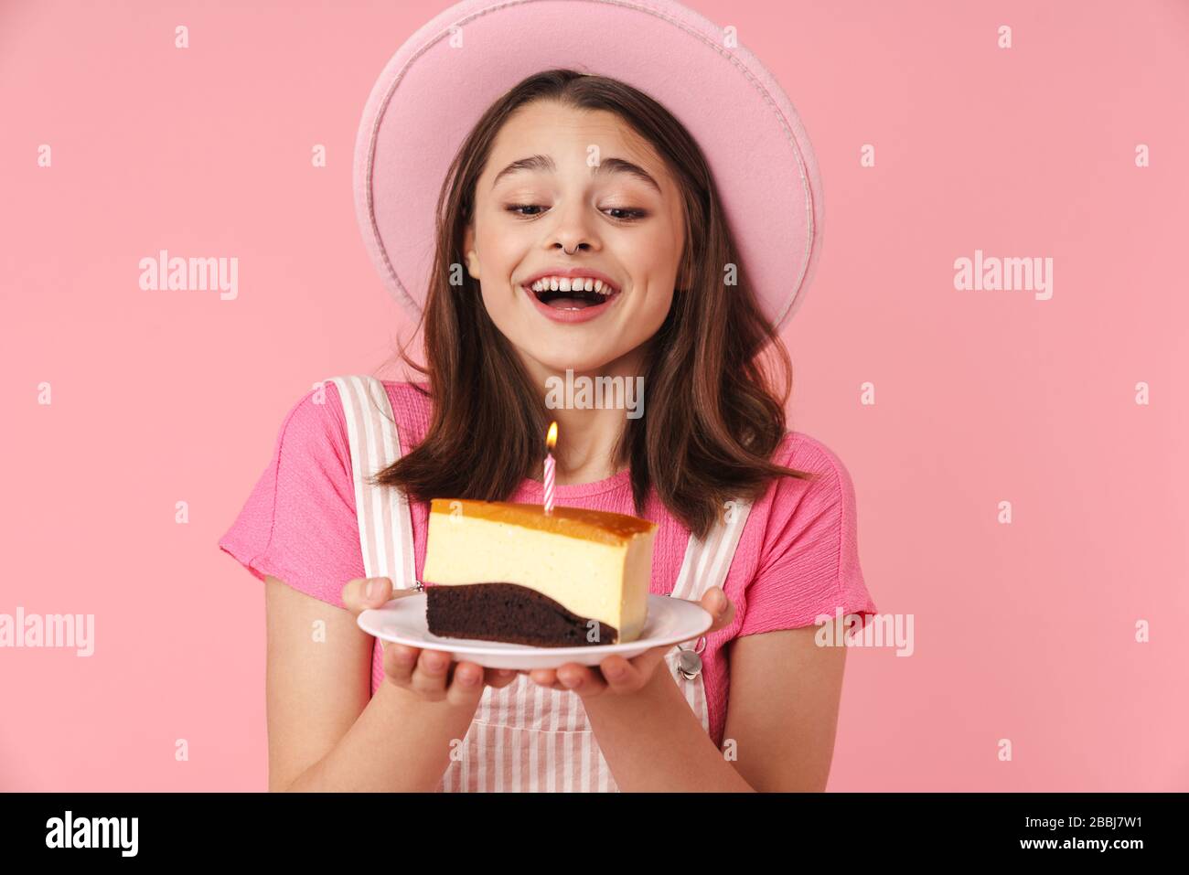 Photo of lovely happy girl in hat holding cake with candle and smiling