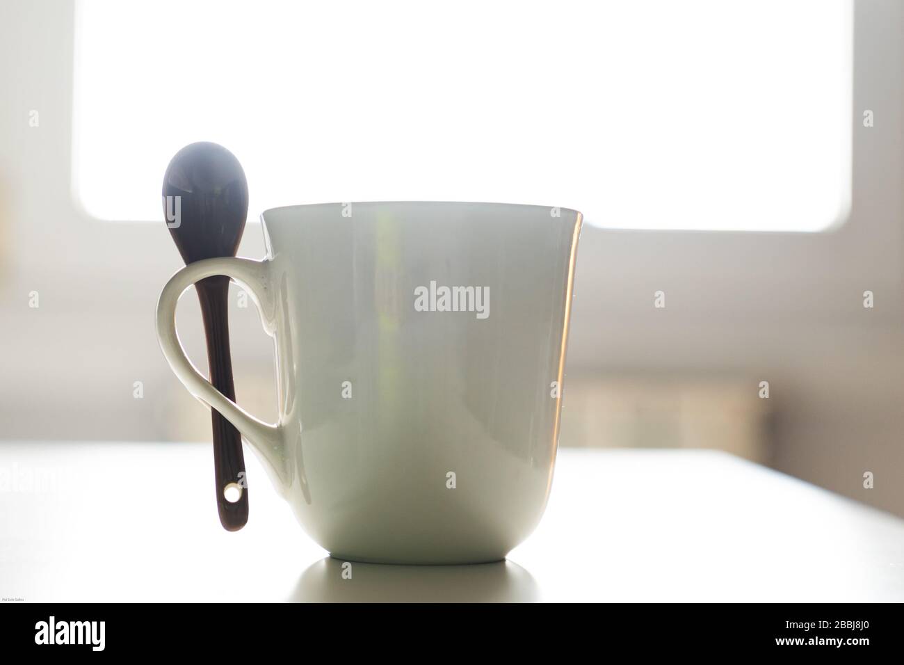 White coffee mug with a spoon with the window light in the background Stock Photo