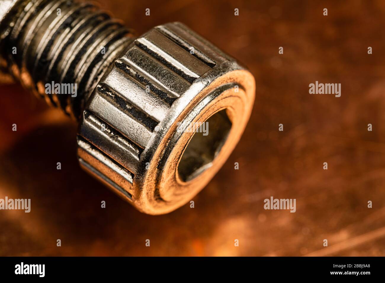 A warm toned macro image of a heavy duty machine thumb screw with an allen wrench hole in the front of it, resting on a worn and oxidized copper work Stock Photo