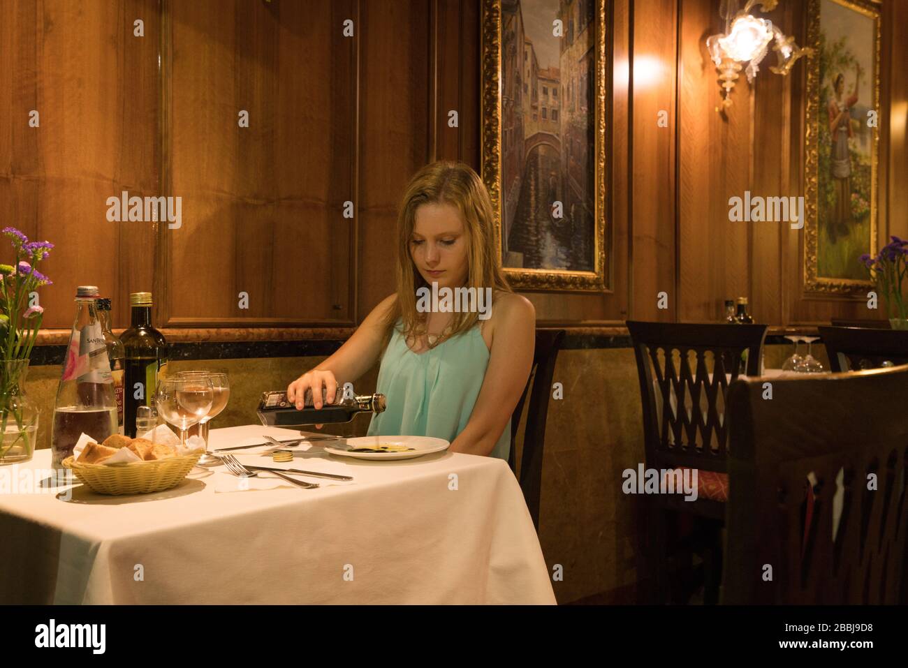 Female pours vinegar on a plate in a restaurant with wood paneling and linen tableclothes near the Rialto Bridge, Venice, Italy Stock Photo