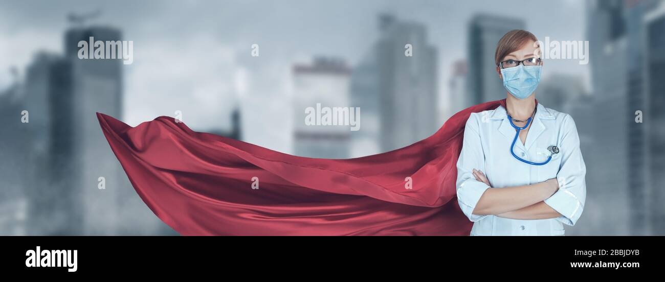 Concept of medical doctors fighting against global pandemic virus. Portrait of young hero woman with super person red cape and medical uniform and mas Stock Photo