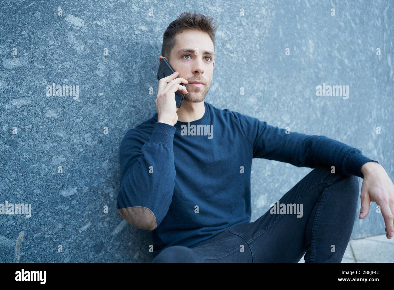 Side view of modern male in casual wear sitting near stone wall and br Stock Photo
