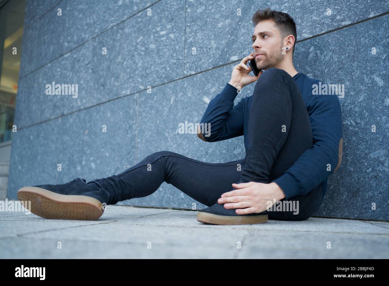 Side view of modern male in casual wear sitting near stone wall and br Stock Photo