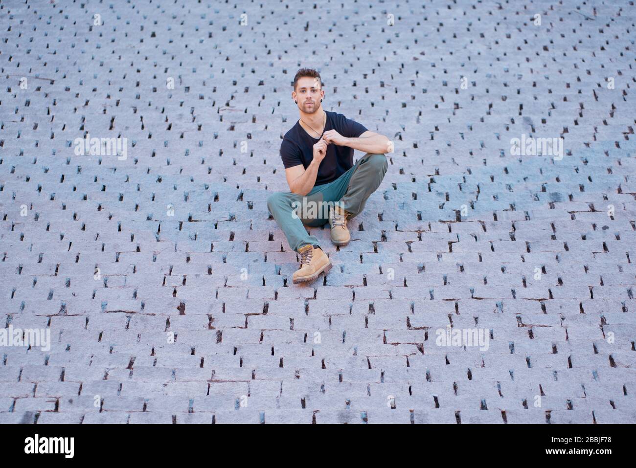 Drontal view of a modern man in casual clothes sitting on some cobbles Stock Photo