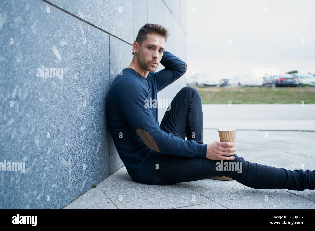 Side view of modern male in casual wear sitting near stone wall and br Stock Photo