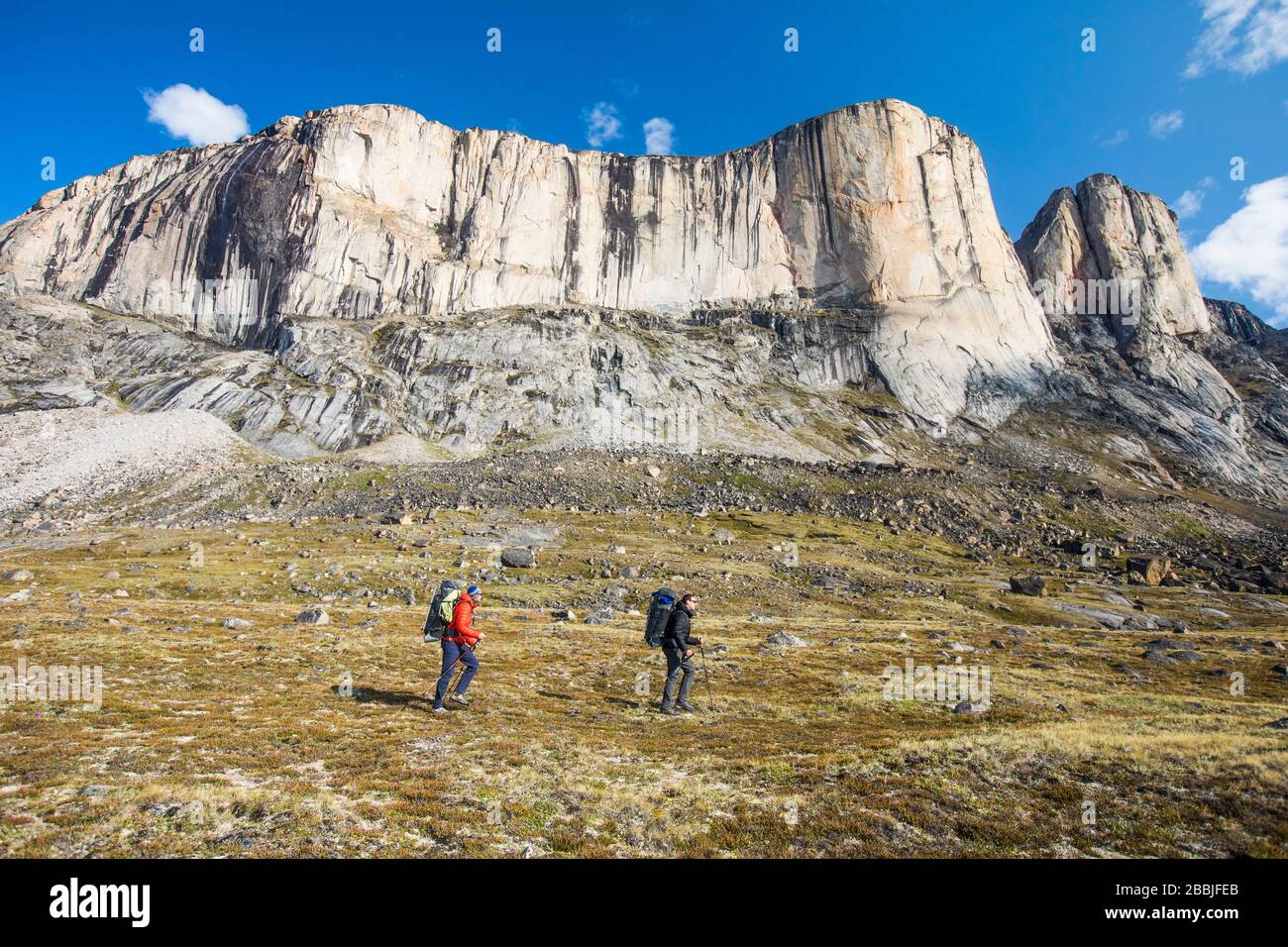 Two backpackers traverse below Baffin Island mountains. Stock Photo