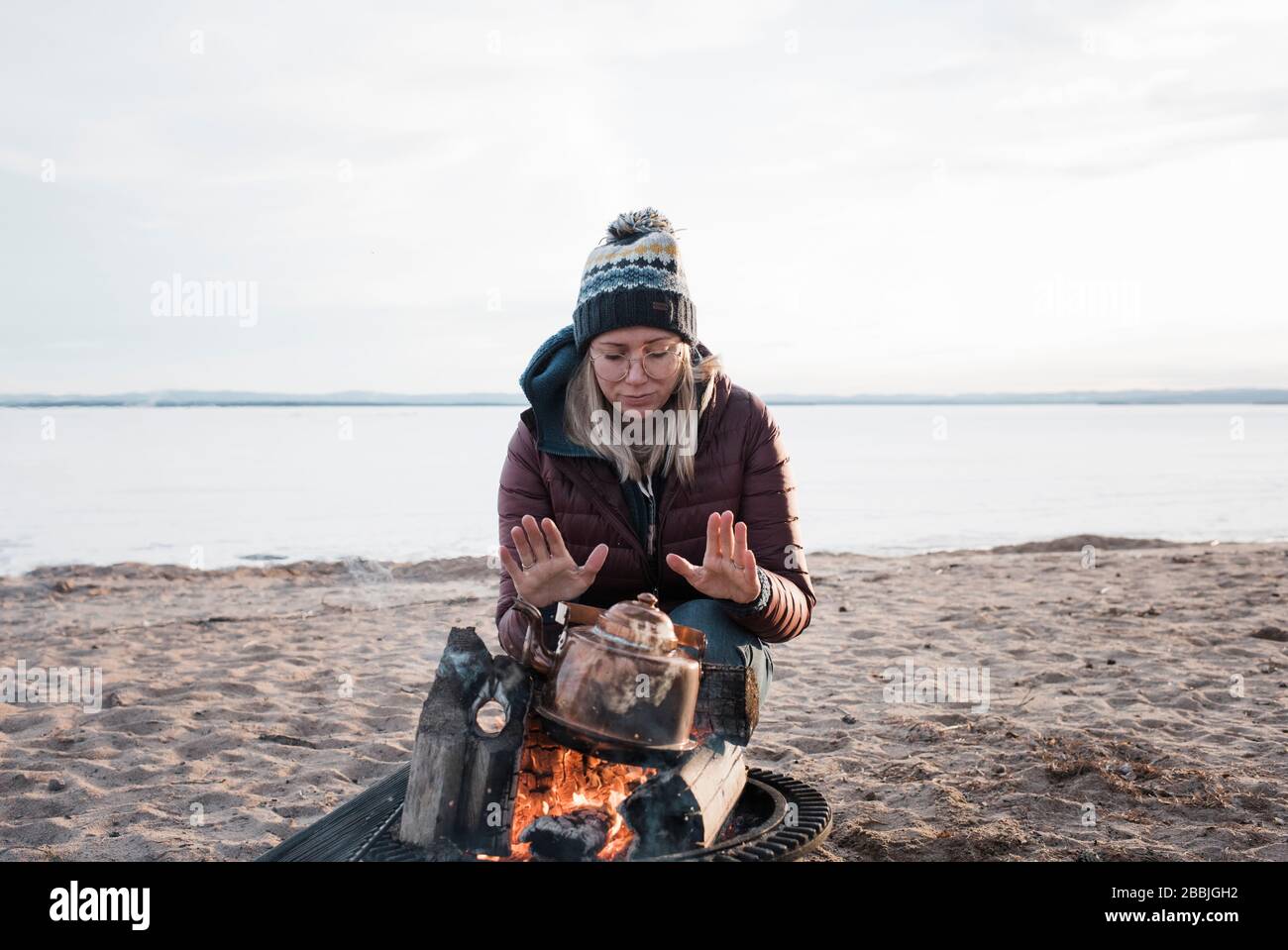woman warming her hands on a camp fire waiting for water to boil Stock Photo