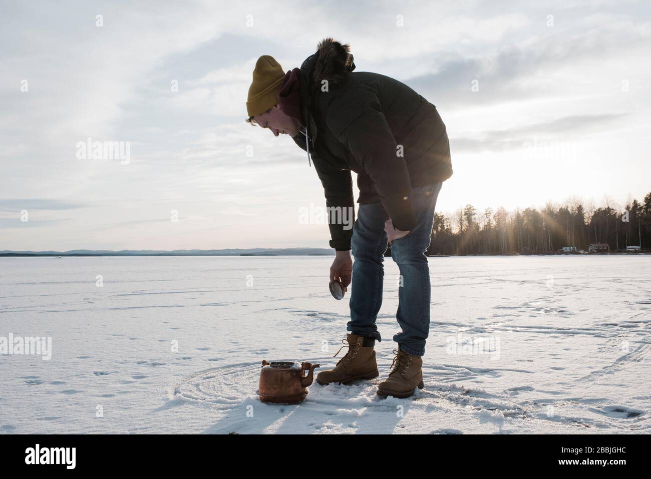 man collecting snow to boil in a kettle on a camp fire whilst camping Stock Photo