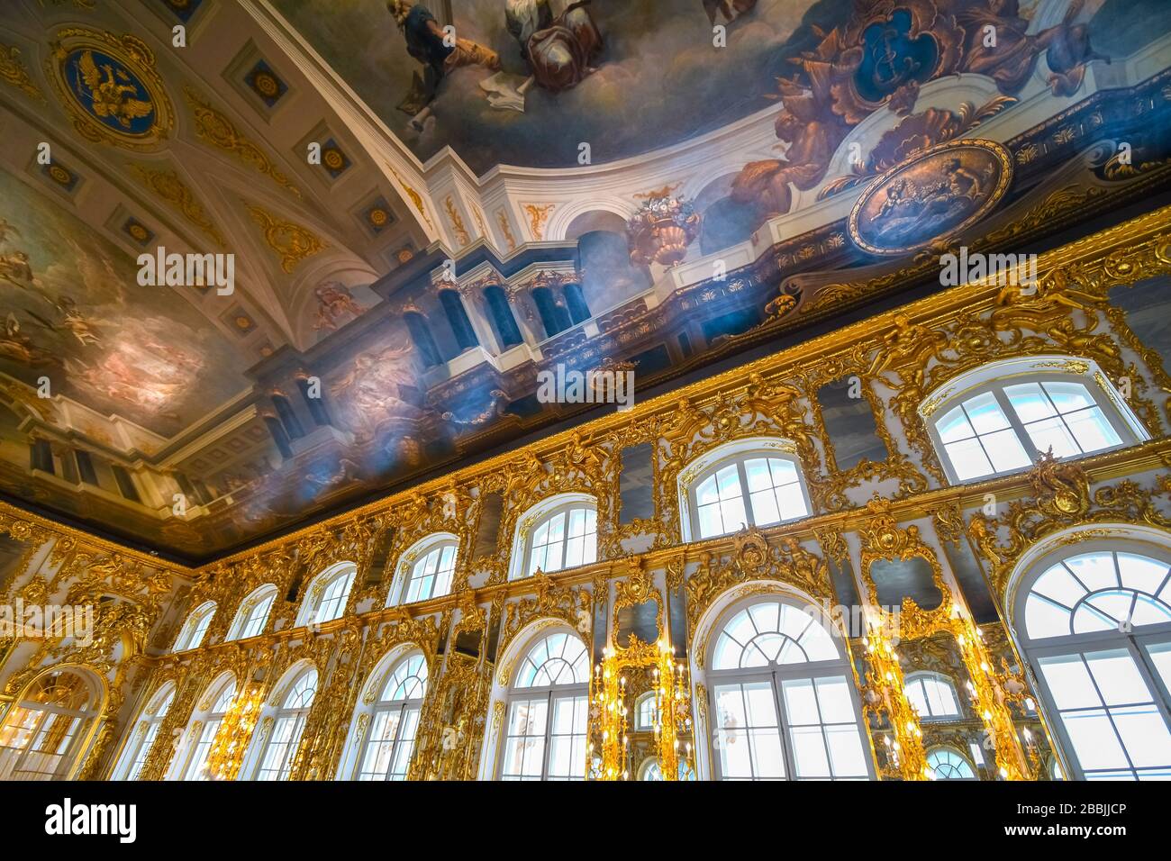 An ornate golden interior ballroom with a colorful painted ceiling inside the Rococo Catherine Palace ballroom at Pushkin near St. Petersburg, Russia. Stock Photo